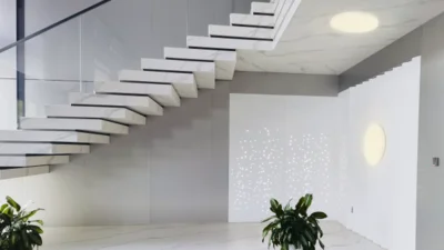 Das Bild zeigt eine moderne Treppe. Unter dem Treppenabsatz und an der Wand unter Treppe sind runde Leuchten angebracht.