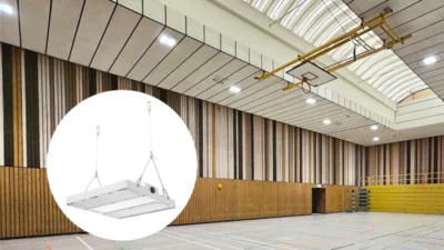 Das Bild zeigt eine moderne Sporthalle mit Holzvertäfelung unterschiedlicher Struktur und Farbe. Unter dem Dach ist ein Basketballnetz an einem Metallgestänge hochgeklappt. Hallenstrahler der Serie Lightbeam beleuchten den Raum. In der linken unteren Bild-Ecke ist in einem weißen Kreis die Hallenleuchte Lightbeam abgebildet.