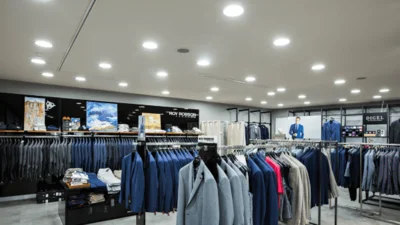 Das Bild zeigt das Innere eines Herrenausstattungsgeschäftes mit verschiedenfarbigen Herrensakkos an im Raum verteilten Kleiderständern. Der Raum wird durch viele runde Downlights UNISIZEevo von Dotlux beleuchtet.
